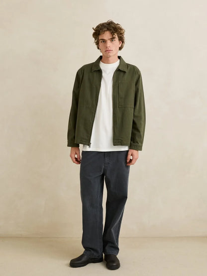 Man wearing a green jacket, white shirt, and dark pants on a beige background