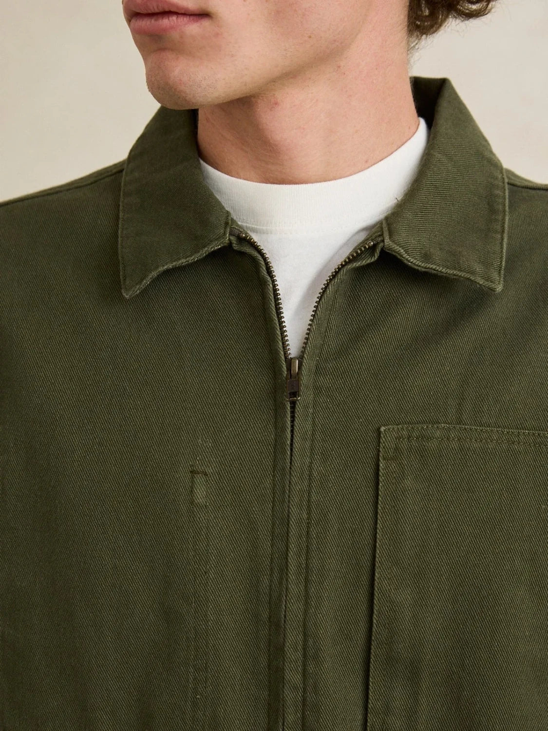 Close-up of a person wearing an olive green jacket with a white shirt underneath.