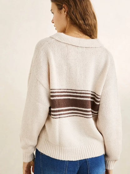 Woman wearing a cream sweater with brown striped pattern on a plain background