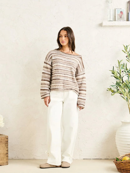 Woman wearing a striped sweater and white pants standing in a room with a plant and basket.