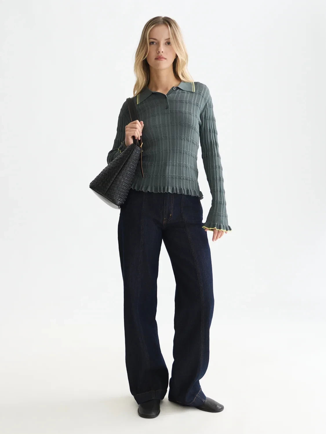 Woman wearing a green plaid shirt and dark pants holding a black handbag on a white background