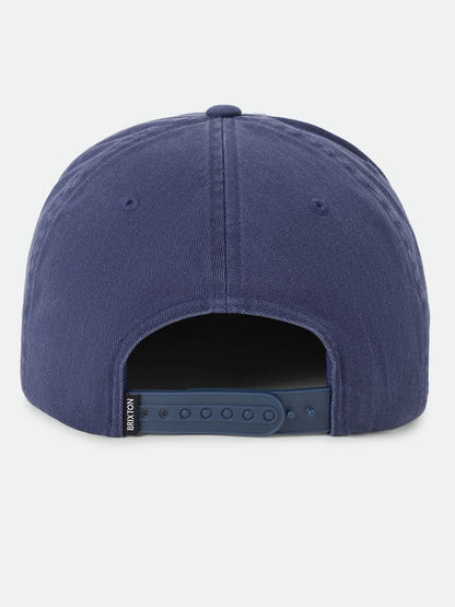 A close-up rear view of a blue snapback cap on a light gray background, showing the fabric crown and adjustable strap.