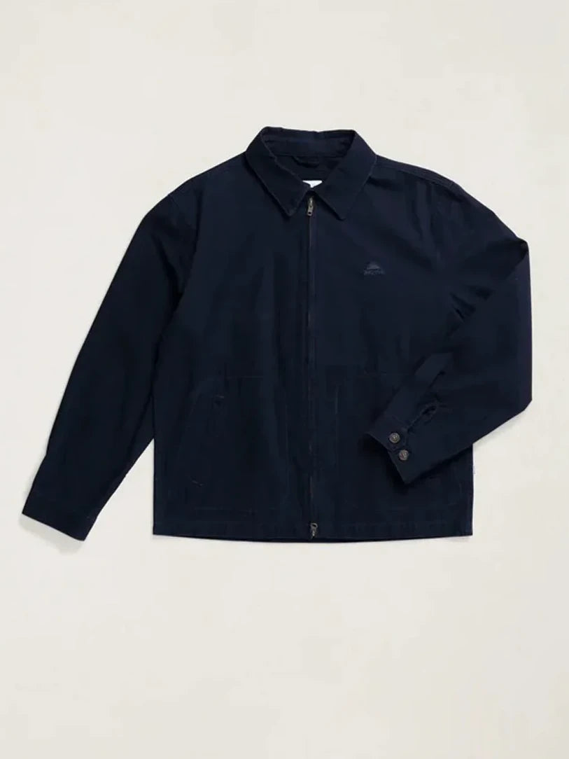 A dark navy blue zip-up jacket with a pointed collar and a small embroidered logo on the left chest, displayed flat against a light beige background.